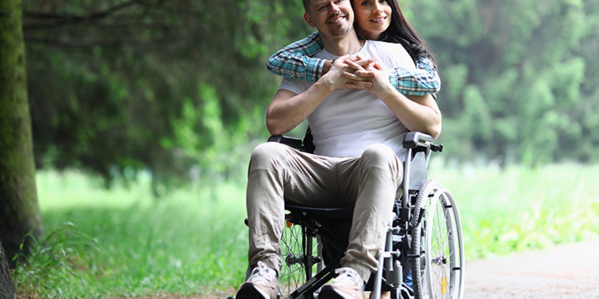 Disabled man sitting in wheelchair from behind hugs beautiful woman. Romantic relationship concept